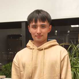 A young man appears in a yellow hoodie, with dark hair and a slight smile