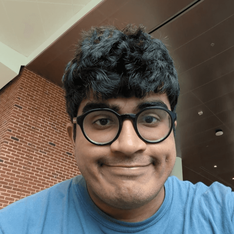 A young man wearing glasses smiles in an interior shot.